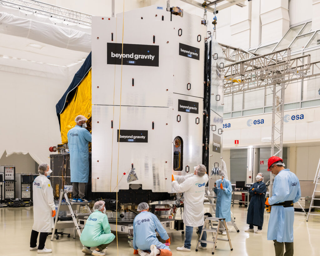 Finalisation de la construction du satellite Plato par les ingénieurs, vue de dos. L'équipe d'ingénieurs a suspendu le module combiné pare-soleil et panneau solaire à l'aide d'un équipement de levage spécial. Elle a ensuite manœuvré le module pour l'aligner précisément avec l'arrière du vaisseau spatial et l'a soigneusement mis en place.